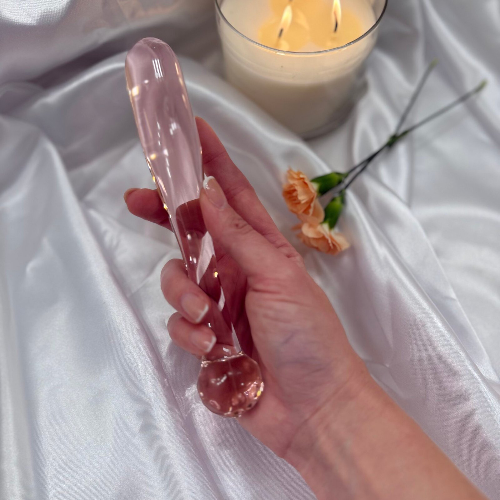 IMG_7439 Elegant rose quartz style glass dildo placed on satin fabric with candle in the background