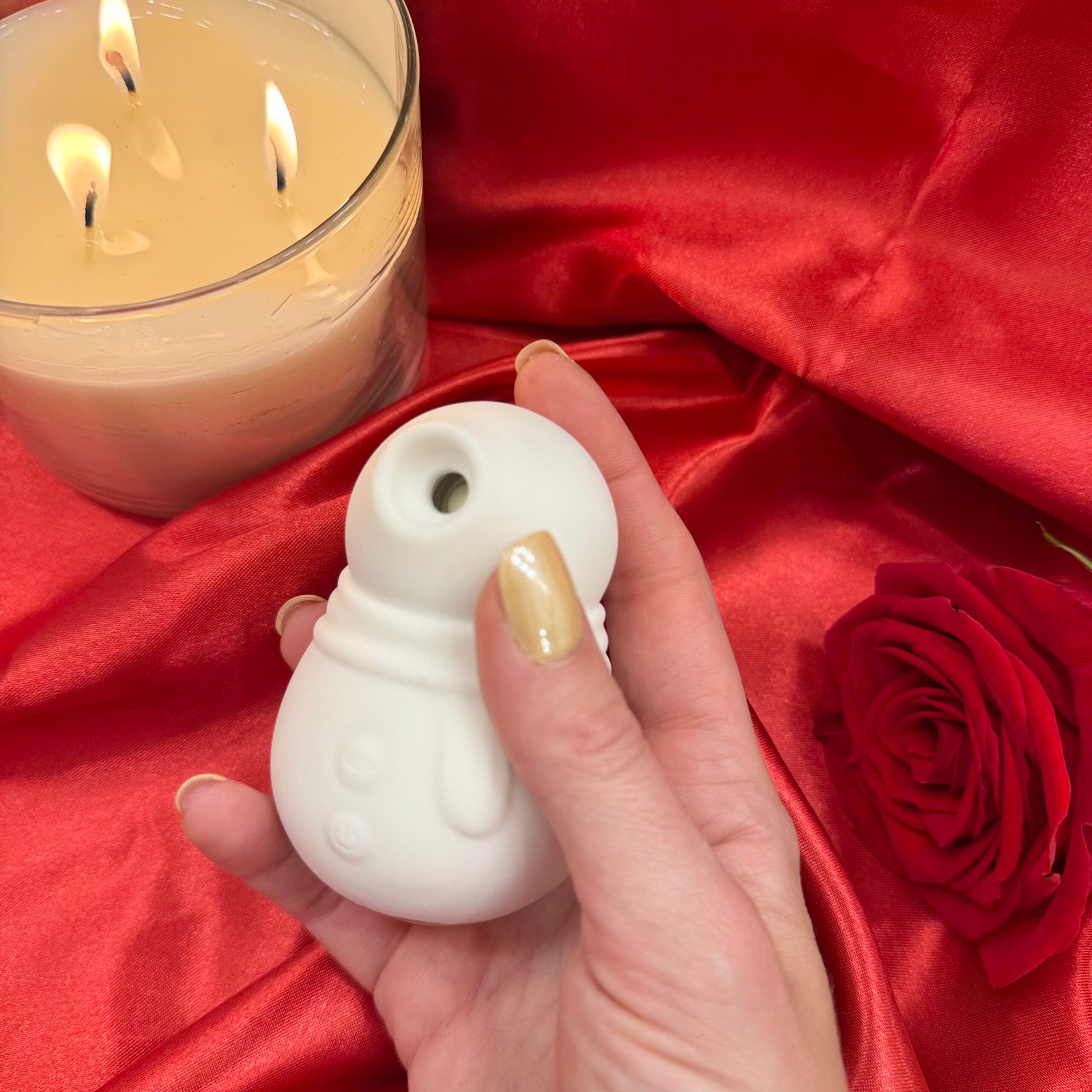 IMG_8522 Snowmen suction vibrator in while silicone, held in hand on red satin background with rose and candle