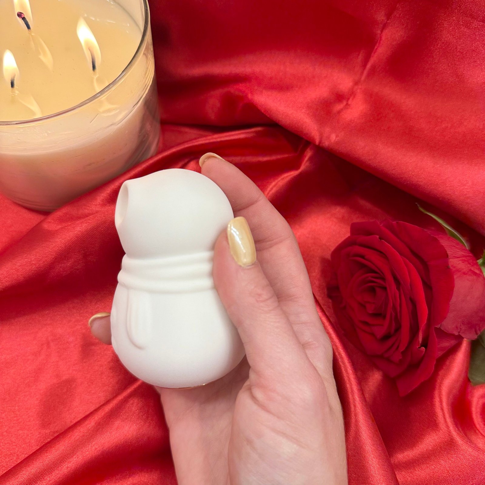 IMG_8524 Snowmen suction vibrator in while silicone, held in hand on red satin background with rose and candle